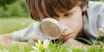 boy looking at daisy through magnifying glass