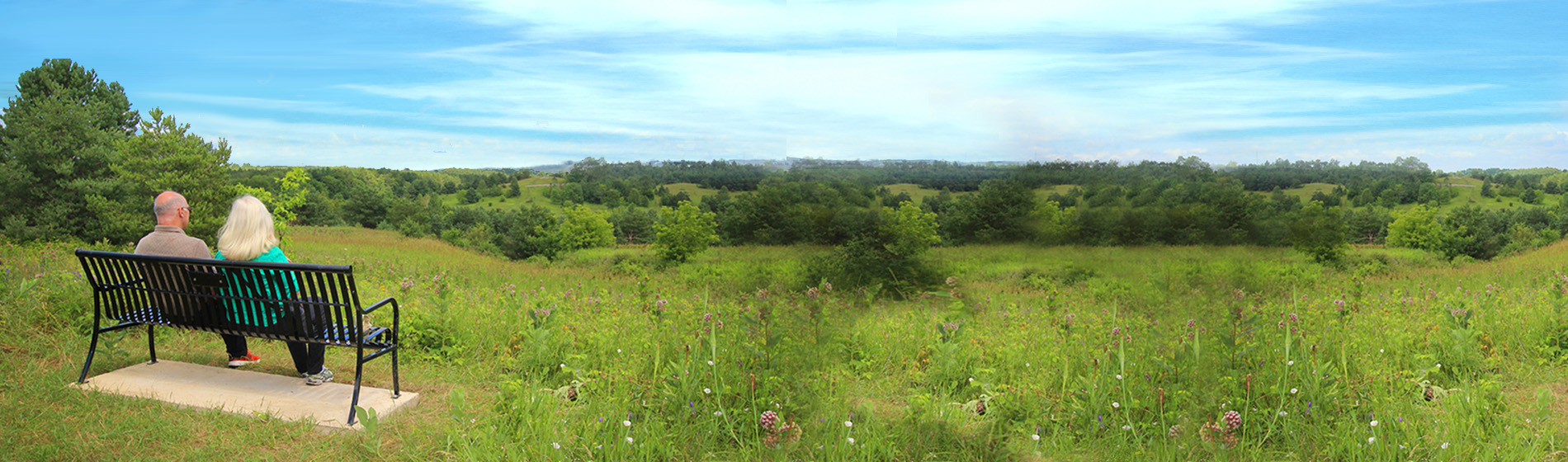 two people sitting on a bench overlooking a field