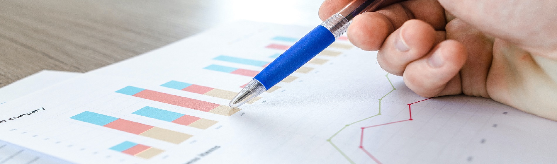 hand holding pen over financial charts