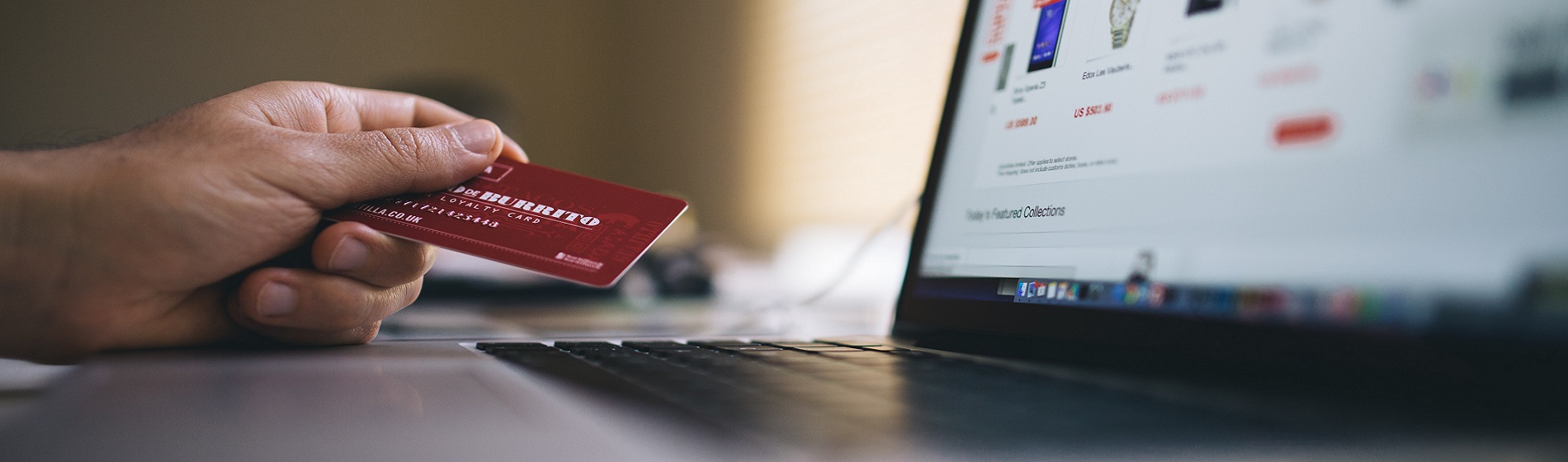 close up of hand holding credit card while sitting at laptop computer